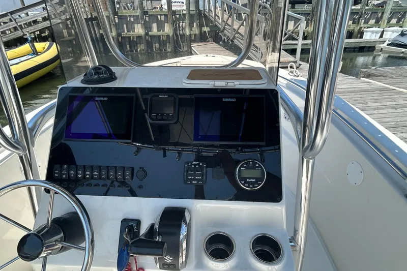 Slide: The Image of 2024 Bulls Bay 230 CC boat dashboard with navigation screens and controls at a marina. - 6