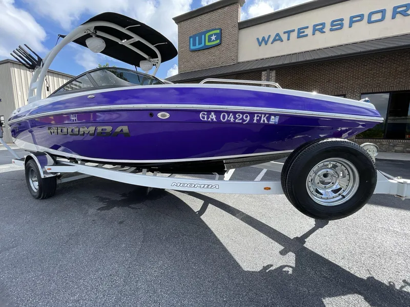 Slide: The Image of 2015 Moomba Mobius LSV boat in vibrant purple on a trailer outside a watersports store. - 2