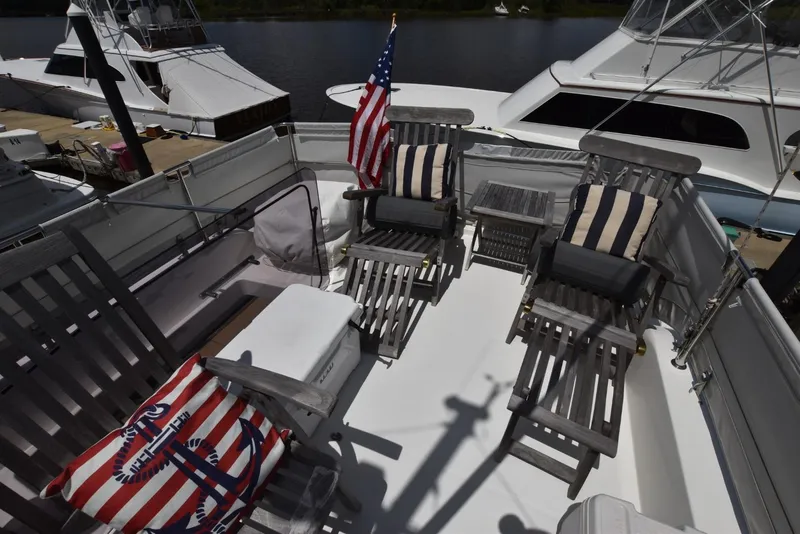 Slide: The Image of 2019 Beneteau Swift Trawler 44 deck with wooden chairs, striped cushions, and American flag. - 35