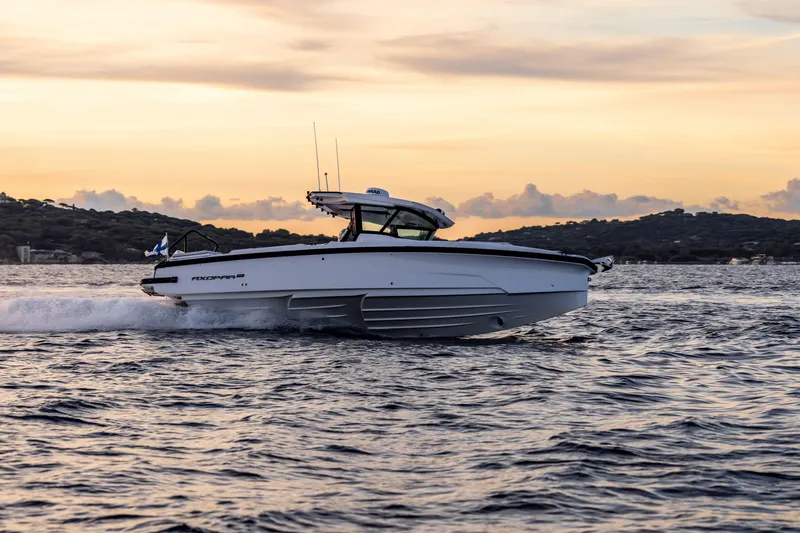 Slide: The Image of 2026 Axopar AX29 CCX boat cruising near urban skyline on a sunny day. - 2