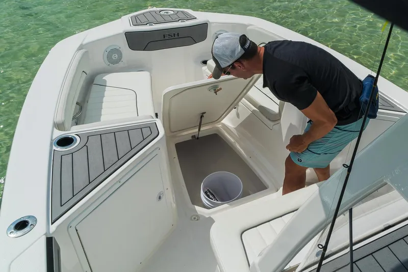 Slide: The Image of Man inspecting storage compartment on 2018 Yamaha Boats 210 FSH Sport in clear water. - 11