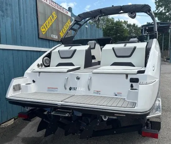 Slide: The Image of 2023 Yamaha Boats 222SD, rear view, white exterior, parked near blue building. - 4