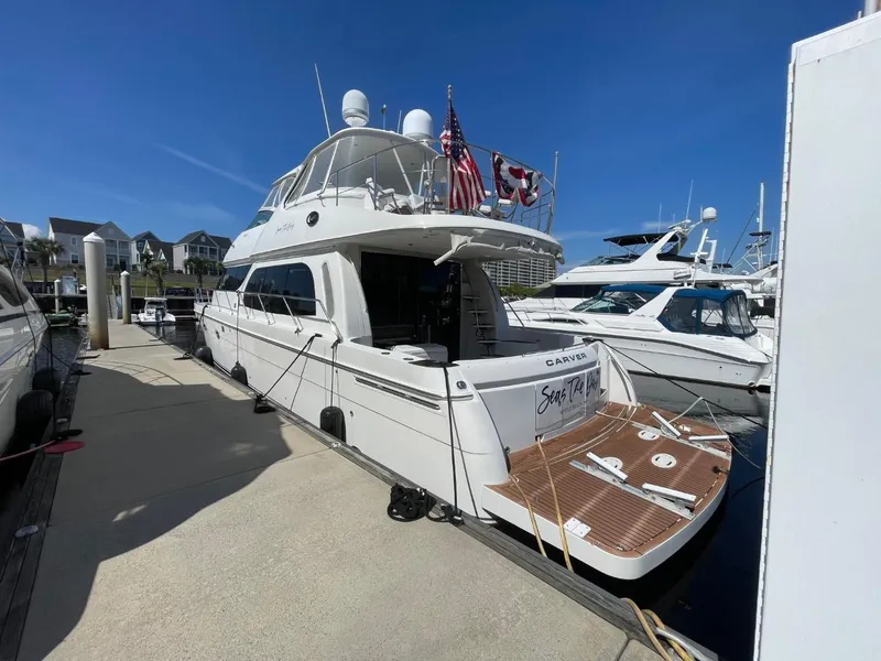 Slide: The Image of 2006 Carver 56 Voyager yacht docked at marina, featuring flags and spacious deck. - 3