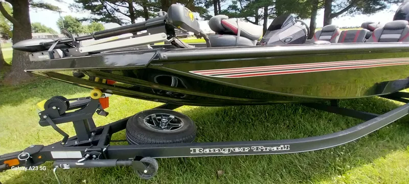 Slide: The Image of 2024 Ranger RT178C boat on trailer, parked on grass, under trees. - 21