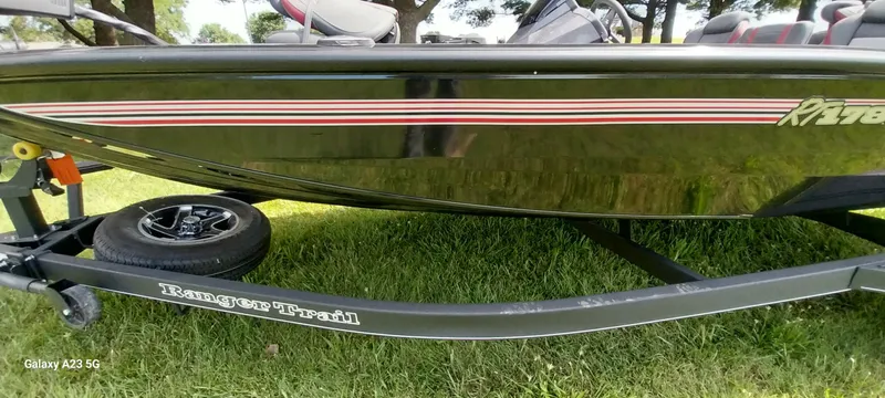 Slide: The Image of 2024 Ranger RT178C boat on trailer, side view with red stripes, parked on grass. - 23