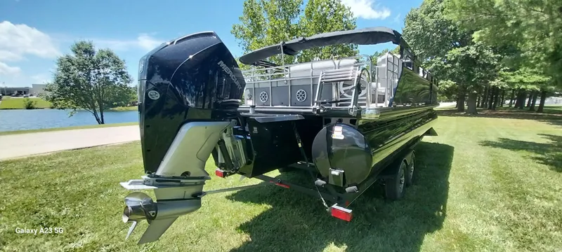 Slide: The Image of 2023 Regency 250 LE3 Sport pontoon boat on grass near a lake, under a clear blue sky. - 12