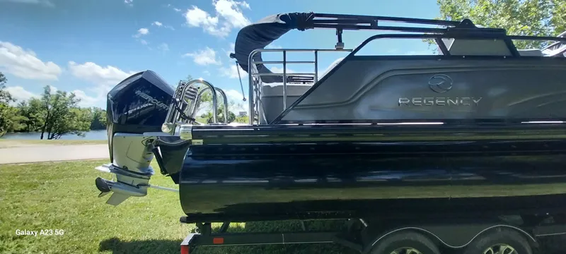Slide: The Image of 2023 Regency 250 LE3 Sport boat with outboard motor, parked on grass near a lake. - 16