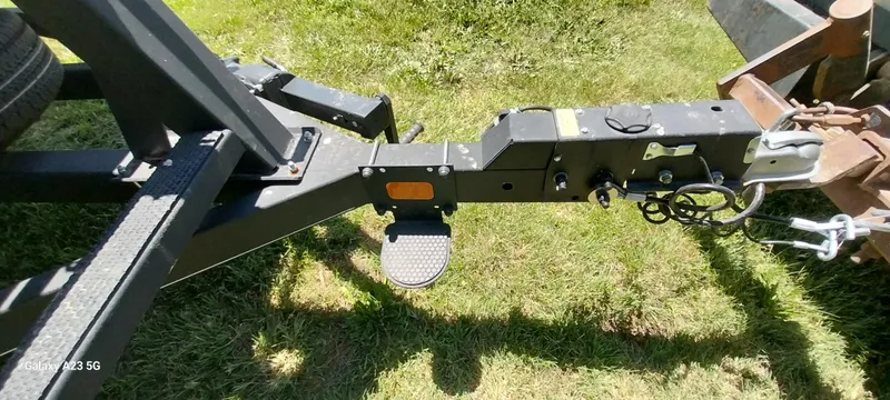 Slide: The Image of Trailer hitch of a 2023 Regency 250 LE3 Sport on grass, showing connections and safety chains. - 22