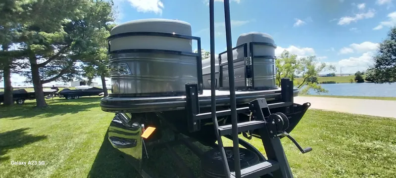 Slide: The Image of 2023 Regency 250 LE3 Sport pontoon boat on grassy lakeside, sunny day. - 23