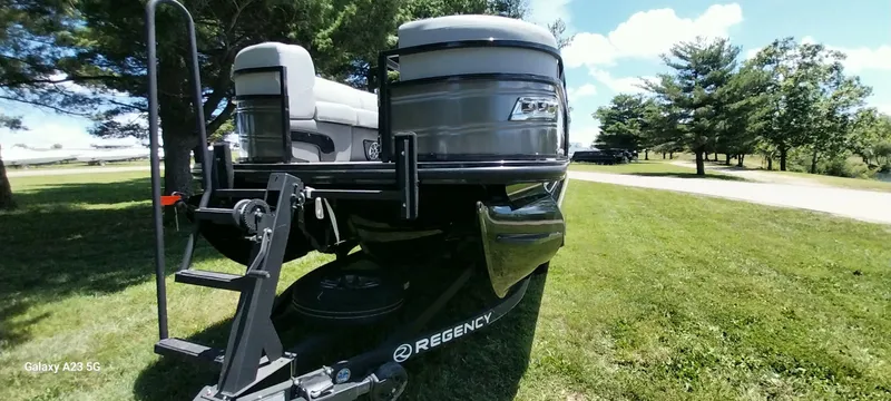 Slide: The Image of 2023 Regency 250 LE3 Sport pontoon boat on trailer, parked on grassy area. - 26