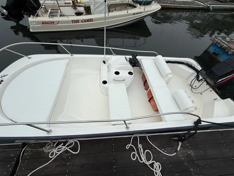 Slide: The Image of 2003 Boston Whaler 150 Sport boat docked, featuring white seating and a clean deck layout. - 1
