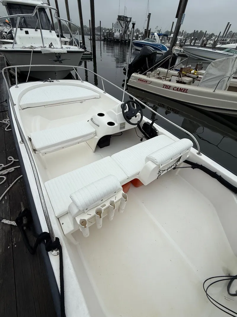 Slide: The Image of 2003 Boston Whaler 150 Sport boat docked, featuring white seating and steering wheel. - 2
