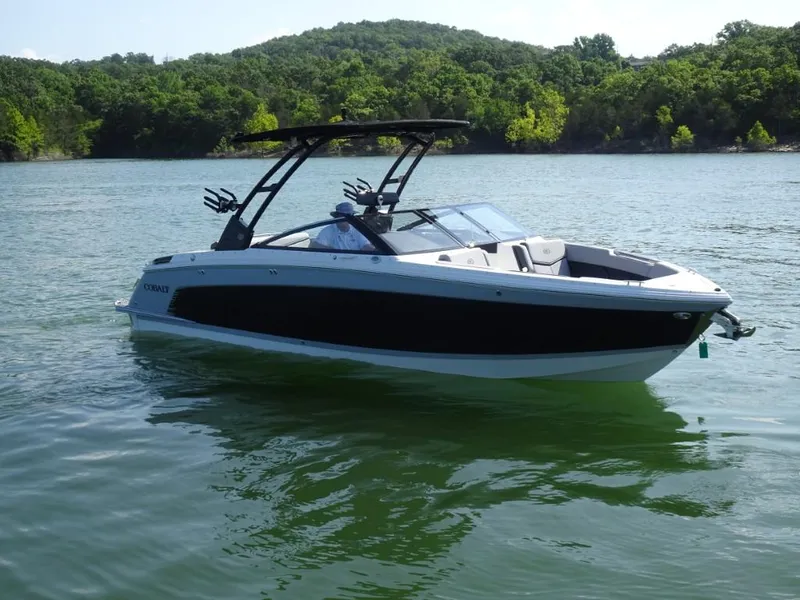 Slide: The Image of 2025 Cobalt R8 Surf boat on a serene lake with lush green hills. - 1