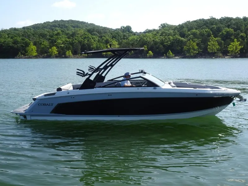 Slide: The Image of 2025 Cobalt R8 Surf boat on a lake with lush green shoreline. - 2