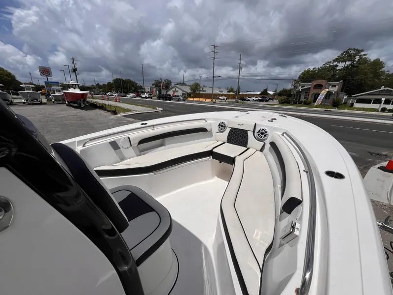 Slide: The Image of 2023 Tidewater 232 LXF boat interior with cushioned seating and speakers, parked outdoors. - 12