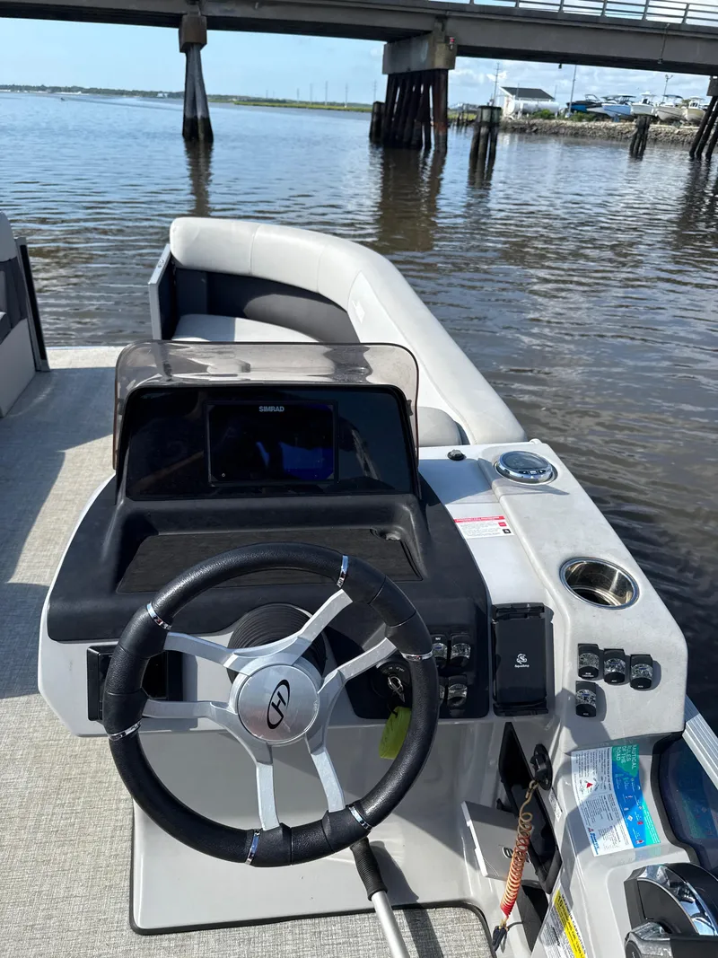 Slide: The Image of 2024 Harris Cruiser 230 boat interior with steering wheel and control panel, docked near a bridge. - 4