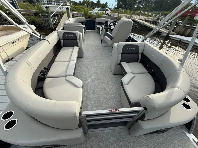 Slide: The Image of 2024 Harris Cruiser 230 pontoon boat with spacious seating and cup holders, docked by the water. - 7