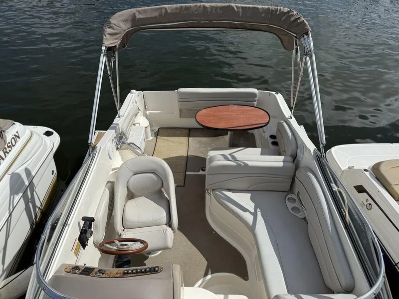 Slide: The Image of 2006 Larson 240 Cabrio boat interior with seating and table, docked on calm water. - 3