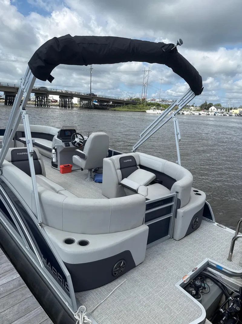 Slide: The Image of 2024 Harris Cruiser 230 pontoon boat with seating, steering console, and canopy on a river. - 2
