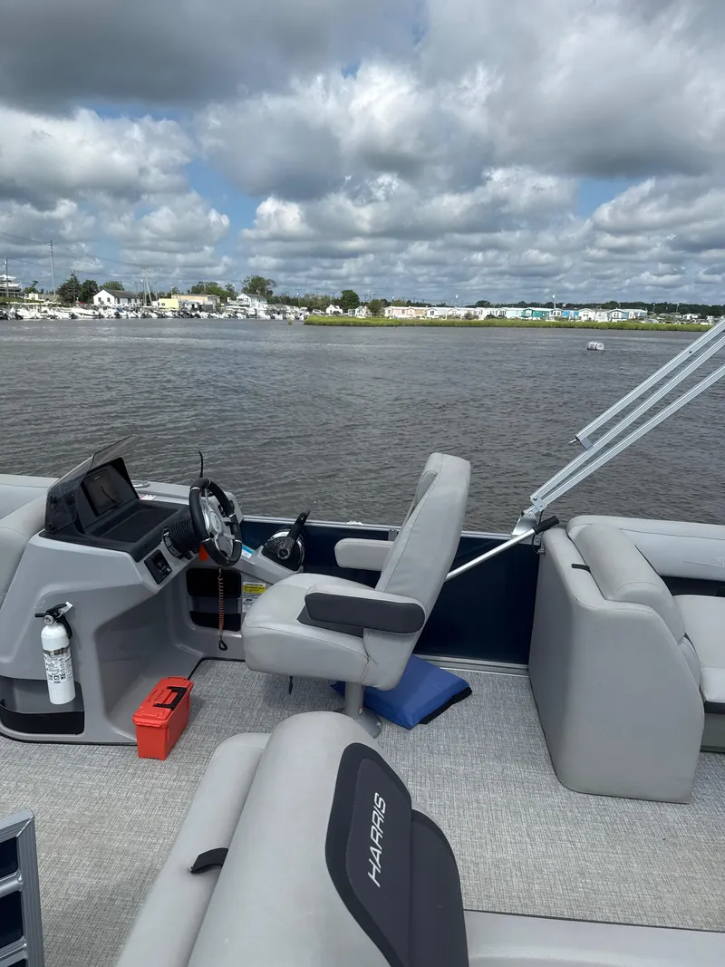 Slide: The Image of 2024 Harris Cruiser 230 pontoon boat interior with steering console, gray seating, and water view. - 3
