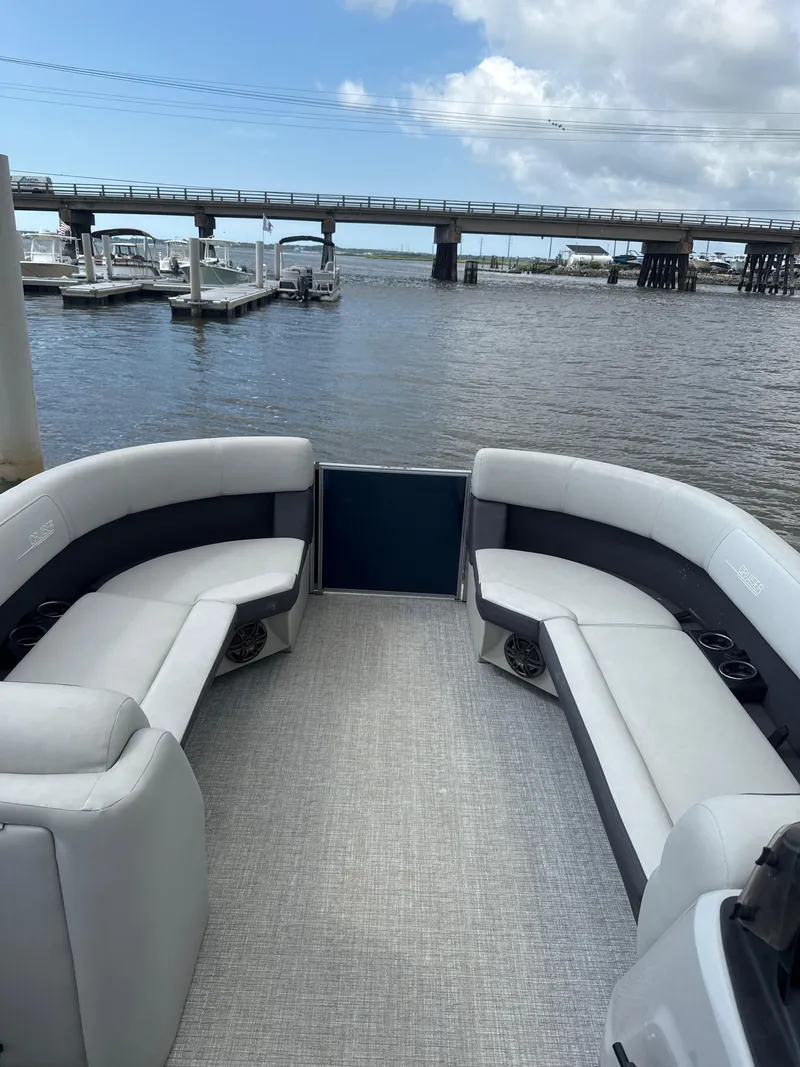 Slide: The Image of 2024 Harris Cruiser 230 pontoon boat interior with plush seating, docked near a bridge. - 6