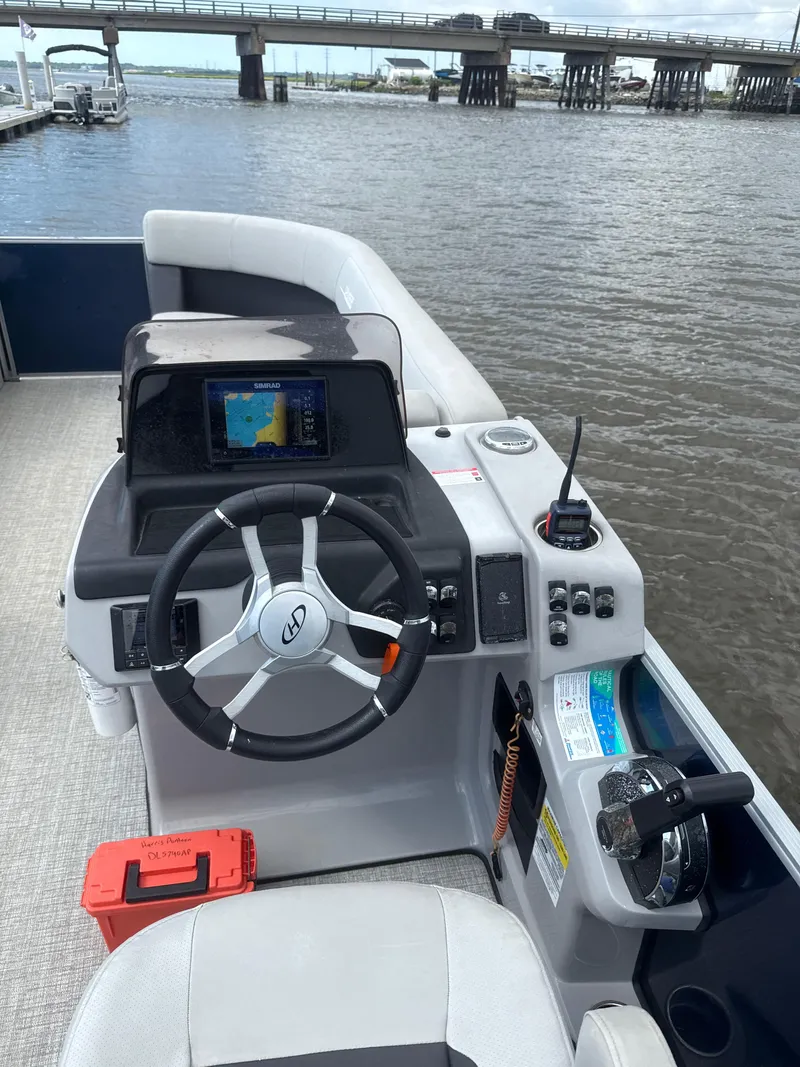 Slide: The Image of 2024 Harris Cruiser 230 boat helm with steering wheel, navigation system, and throttle controls. - 7