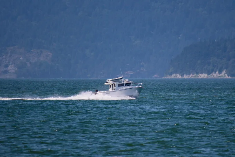 Slide: The Image of Ocean Sport 26/27 boat cruising on a lake, 2021 model, with forested hills in the background. - 3