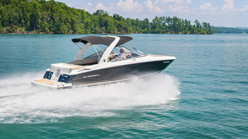 Slide: The Image of 2015 Regal 2700 ES Bowrider speeding on a scenic lake with lush green shoreline. - 2