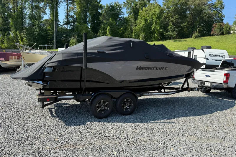 Slide: The Image of 2020 MasterCraft X22 boat covered on trailer, parked outdoors on gravel. - 3