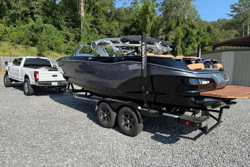 Slide: The Image of 2020 MasterCraft X22 boat on trailer, hitched to a white truck, parked on gravel. - 5