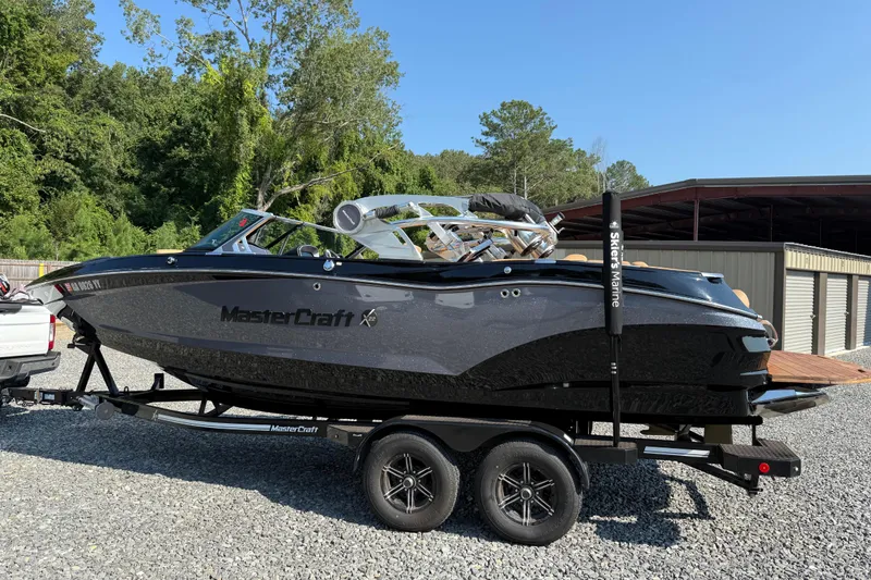Slide: The Image of 2020 MasterCraft X22 boat on trailer, parked outdoors near trees and storage building. - 6