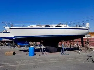 Slide: The Image of 1987 Ericson 34 2 sailboat on stands in a boatyard under clear blue sky. - 27