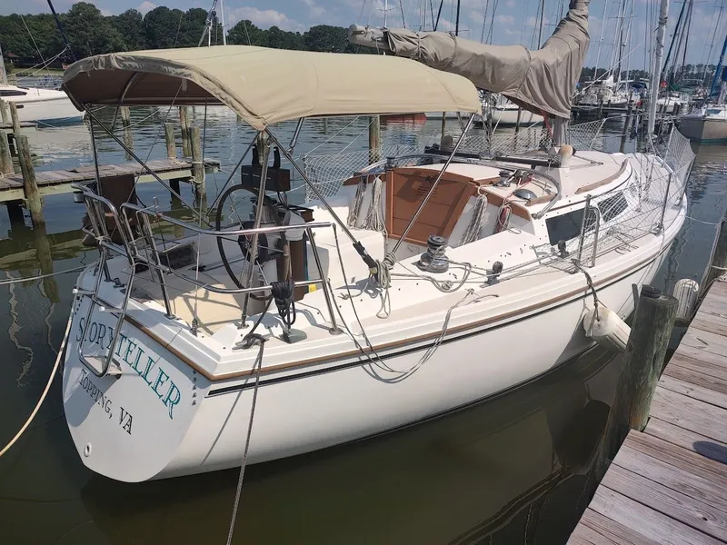 Slide: The Image of 1986 Catalina C-34 sailboat docked at marina, featuring beige canopy and wooden deck. - 2