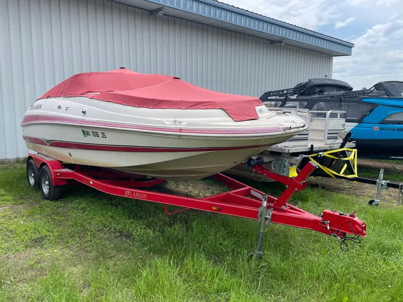 Slide: The Image of 2003 Larson 214 boat on red trailer, covered, parked beside a building. - 0