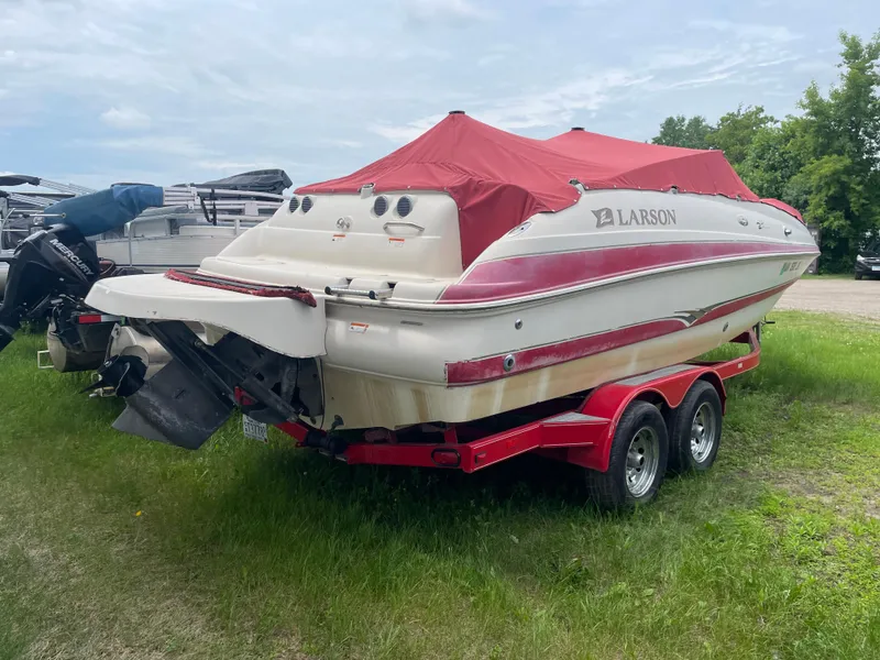 Slide: The Image of 2003 Larson 214 boat with red cover on trailer, parked on grass. - 1