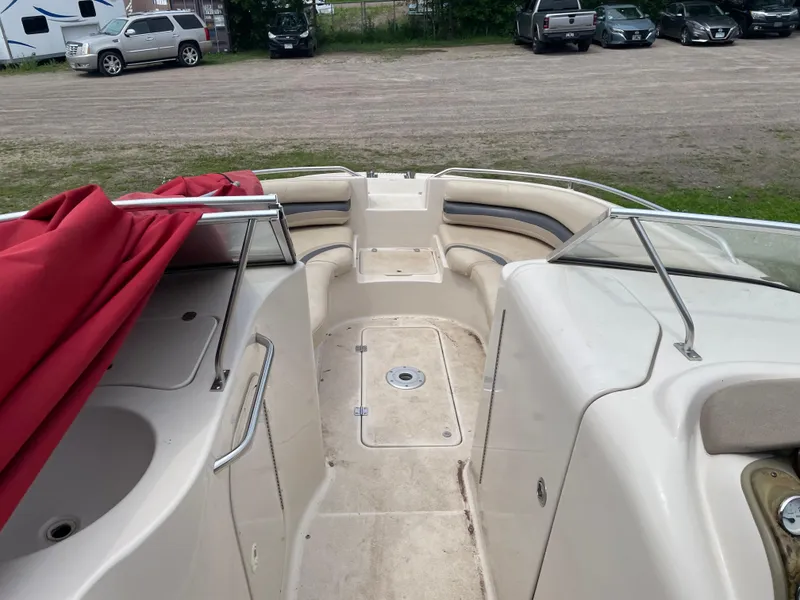 Slide: The Image of 2003 Larson 214 boat interior with red cover, parked near vehicles. - 4