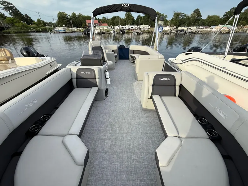 Slide: The Image of 2024 Harris Cruiser 230 pontoon boat interior with gray seating, docked by a calm lake. - 5