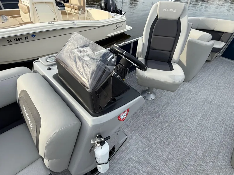 Slide: The Image of 2024 Harris Cruiser 230 boat interior with steering console and seating, docked near water. - 6