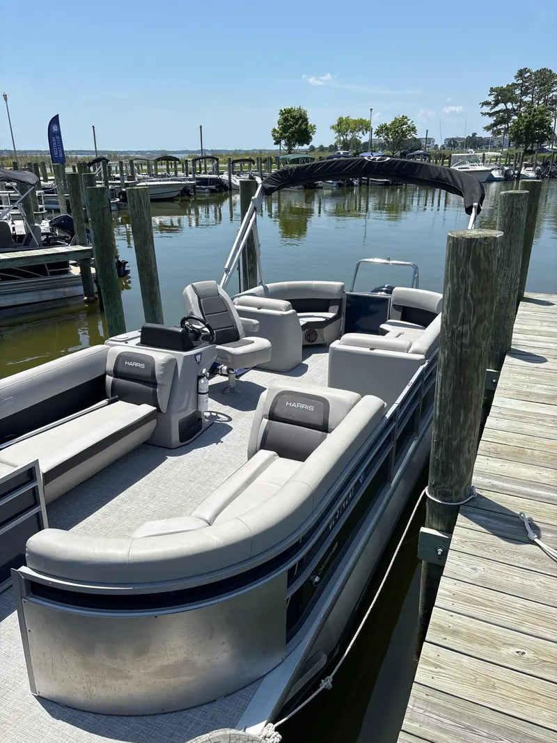 Slide: The Image of 2024 Harris Cruiser 230 pontoon boat docked at a marina on a sunny day. - 2