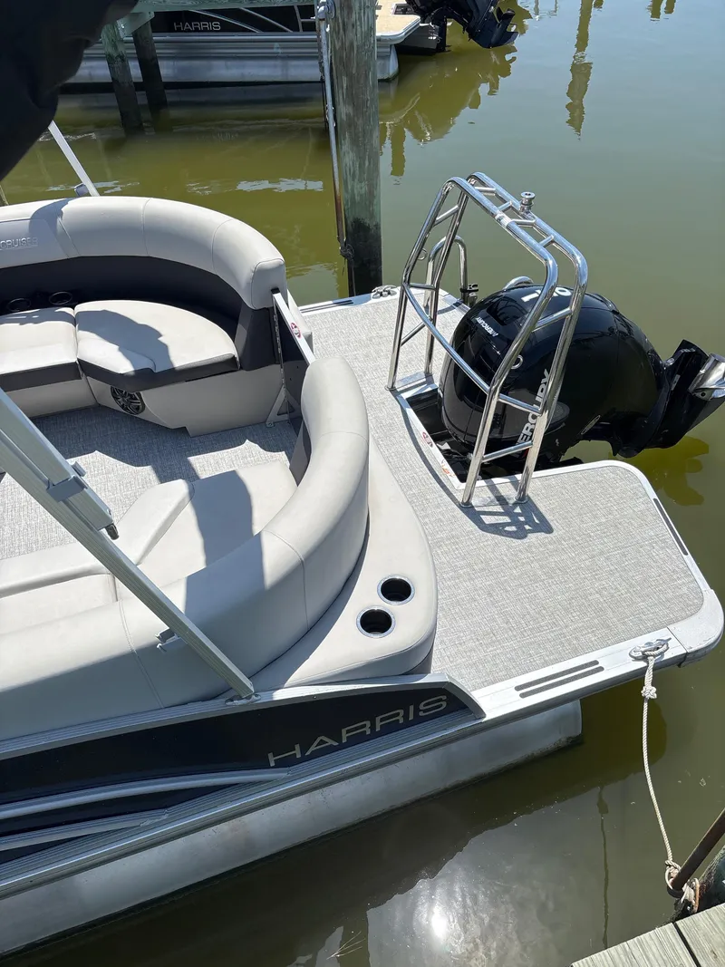 Slide: The Image of 2024 Harris Cruiser 230 pontoon boat with seating and outboard motor, docked on calm water. - 4