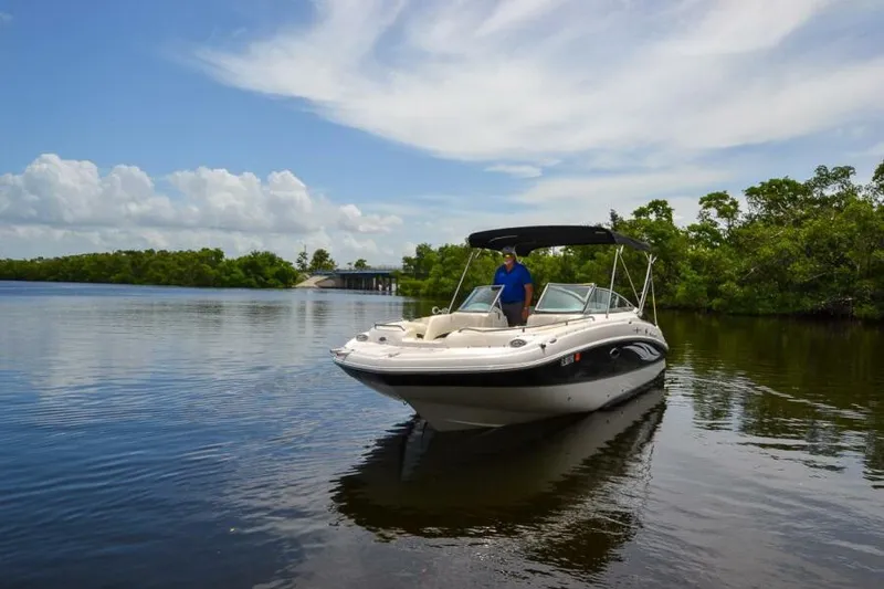 Slide: The Image of 2011 Sea Ray 240 Sundeck boat on calm water, with lush greenery and blue sky. - 2