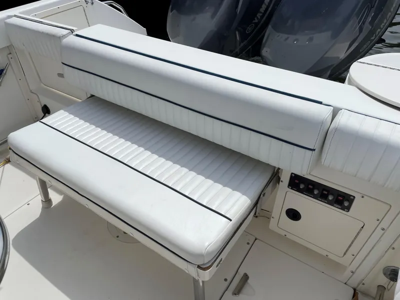 Slide: The Image of 1999 Boston Whaler Outrage 23 boat seating area with white cushioned bench and control panel. - 15