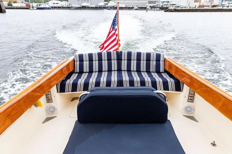 Slide: The Image of 1998 Hinckley Picnic Boat with striped seating and American flag on open water. - 19