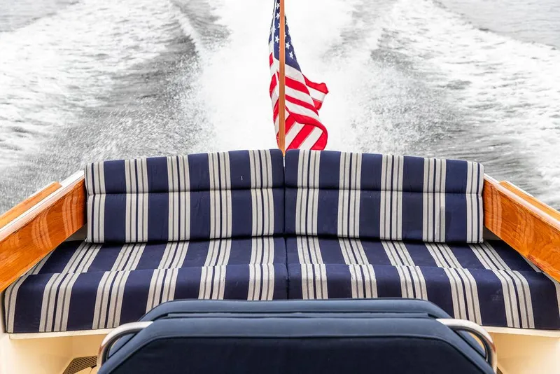 Slide: The Image of 1998 Hinckley Picnic Boat with striped seating and American flag, cruising on water. - 20