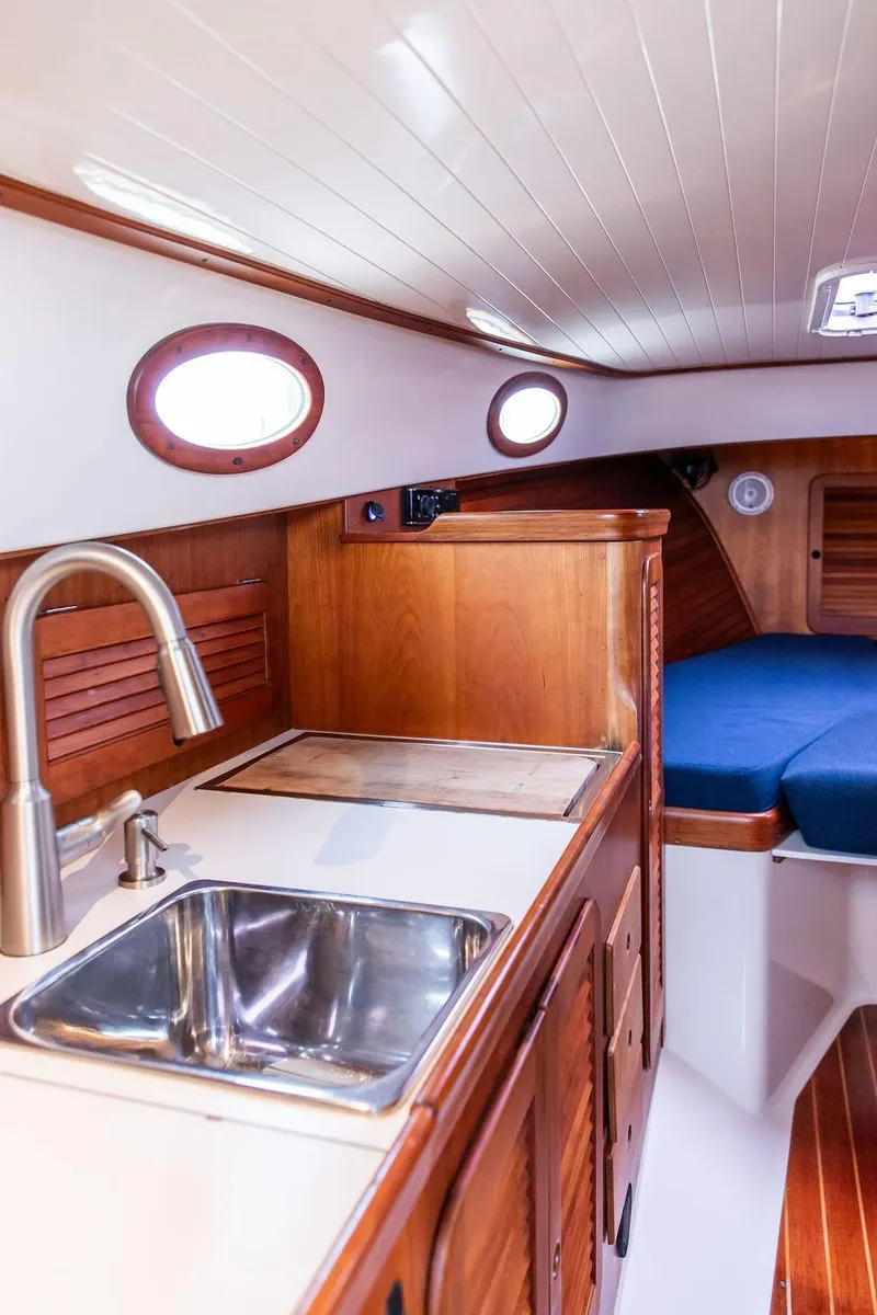 Slide: The Image of 1998 Hinckley Picnic Boat interior with wooden cabinetry, sink, and blue seating. - 34