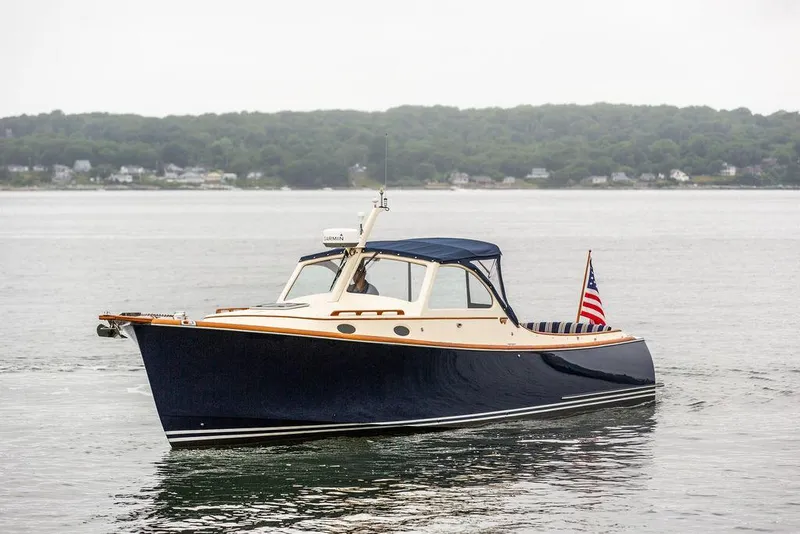 Slide: The Image of 1998 Hinckley Picnic Boat on calm water with American flag, scenic shoreline background. - 11