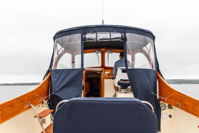Slide: The Image of 1998 Hinckley Picnic Boat interior with wooden accents and blue canopy on a calm waterway. - 23