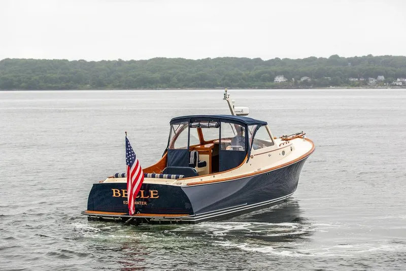 Slide: The Image of 1998 Hinckley Picnic Boat on water, displaying American flag, with lush shoreline in background. - 3