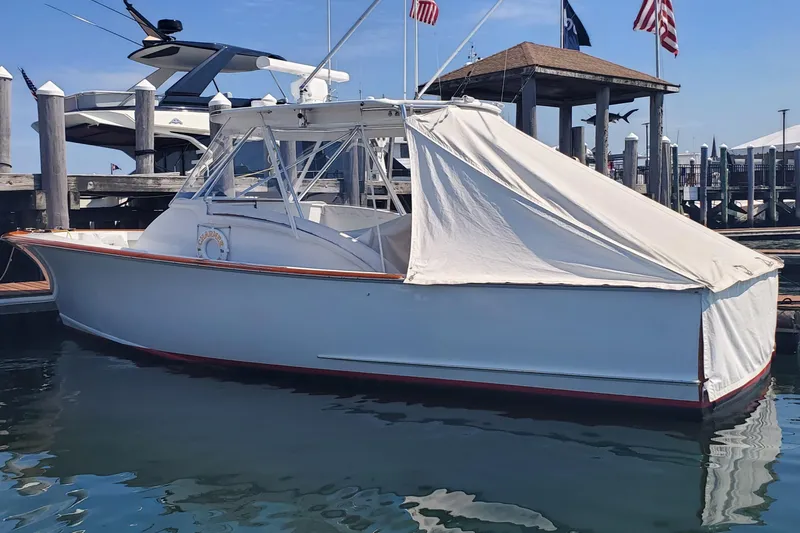 Slide: The Image of 1985 Rybovich 32 Express Walkaround Sportfish docked with cover, flags in background. - 2