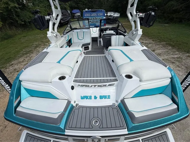 Slide: The Image of 2020 Nautique Super Air Nautique G21 boat with white and teal seating, docked on grass. - 7